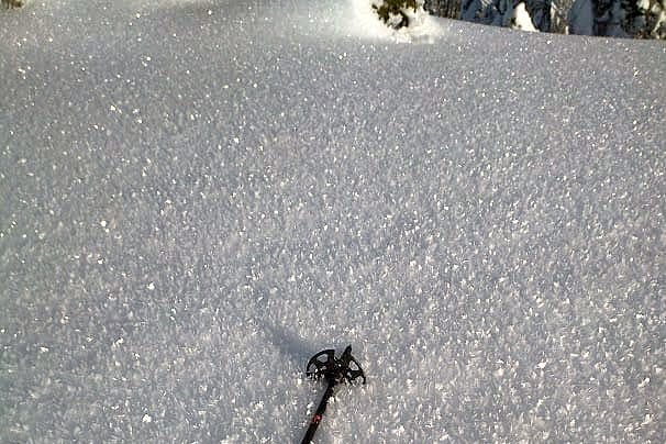 A ski pole rests on the snow surface covered with large surface hoar crystals