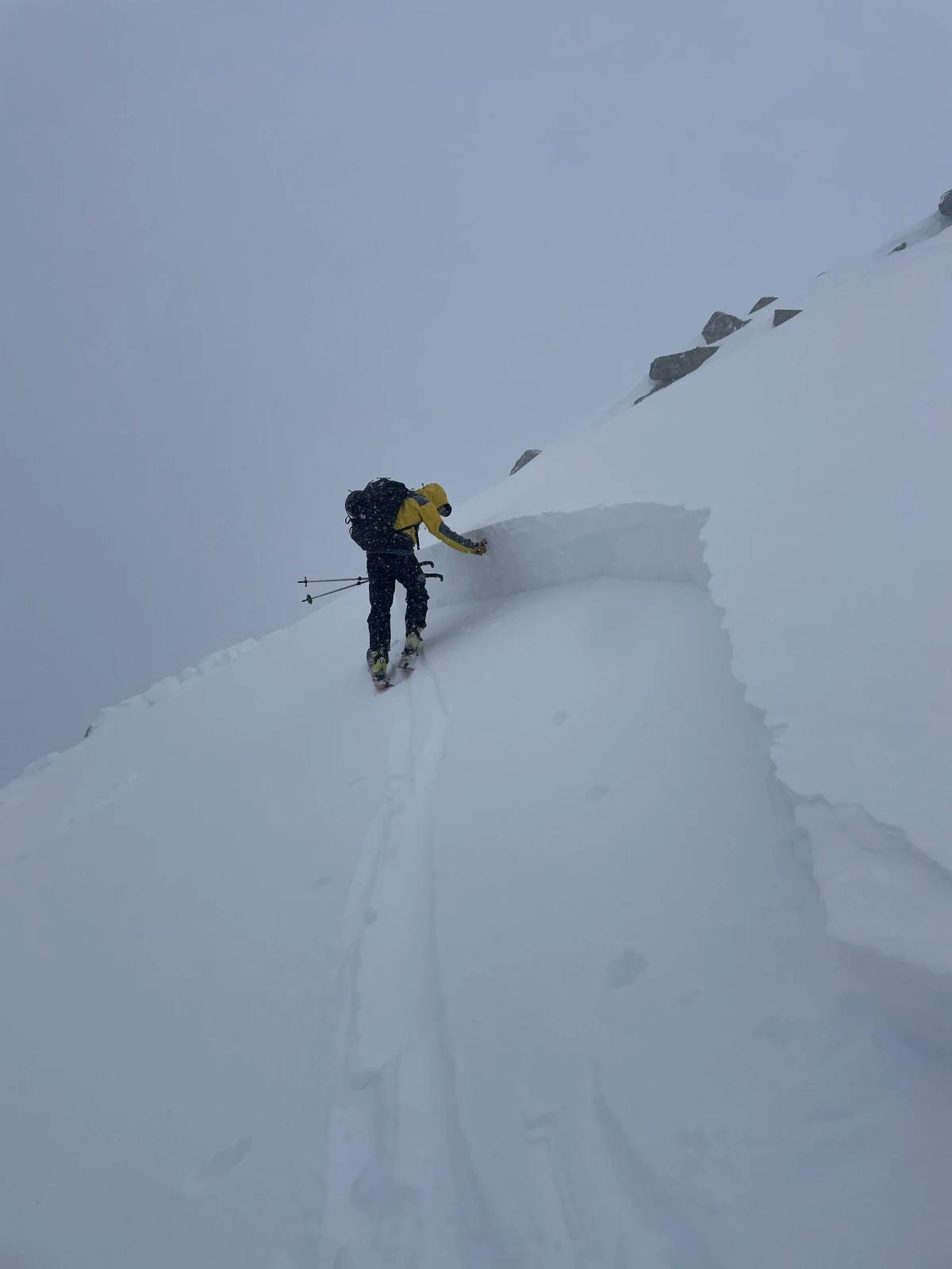 A skier standing underneath waist-high avalanche crown. 