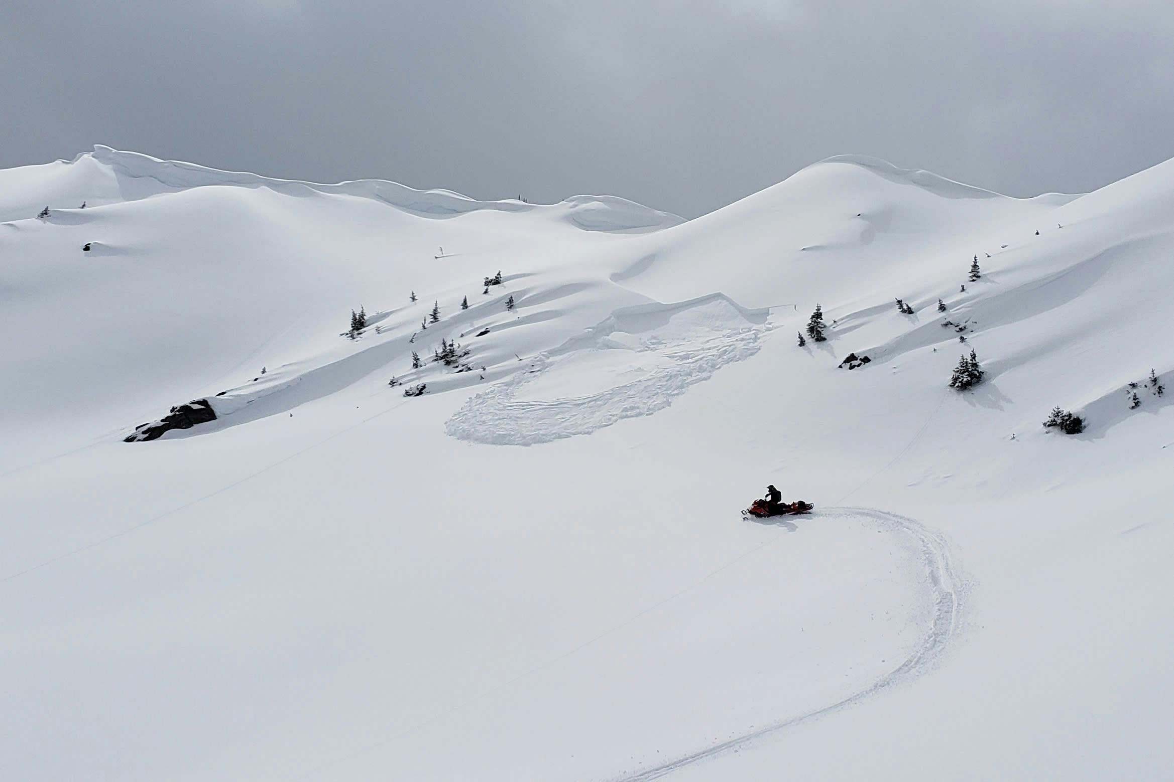 A snowmobile triggers a remote slab avalanche several feet from the sled. 