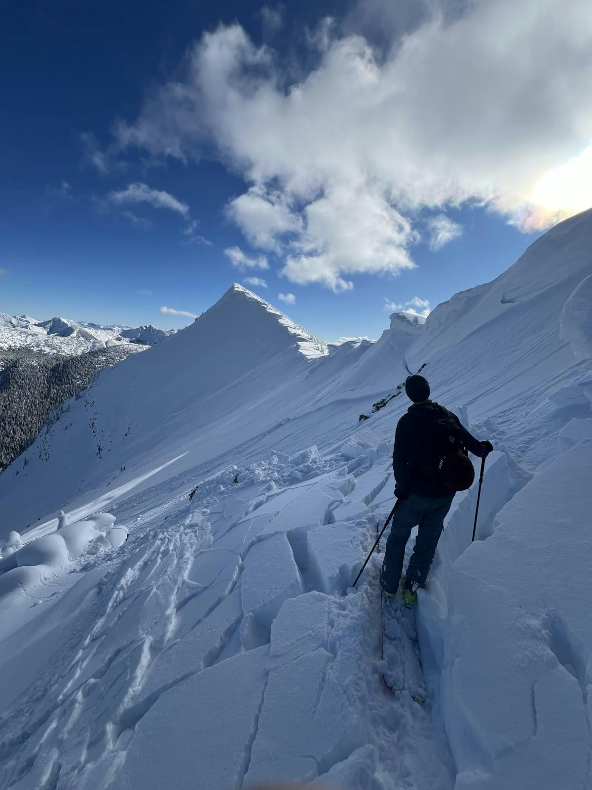 A person ski touring near ridgetop standing among blocks of snow that have broken into an avalanche 