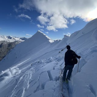 A person ski touring near ridgetop standing among blocks of snow that have broken into an avalanche