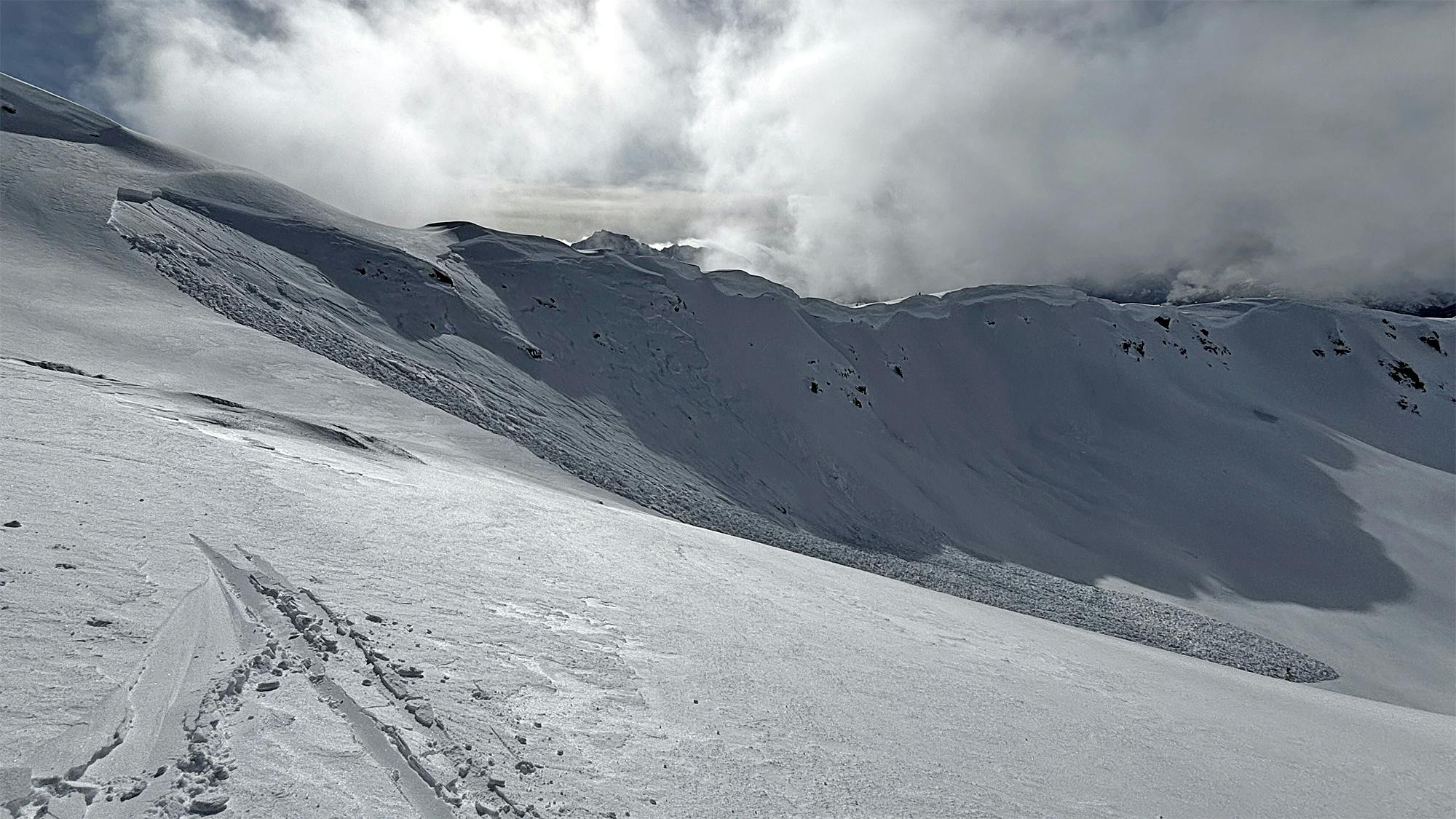 ski tracks in foreground and avalanche on steeper alpine slope in background