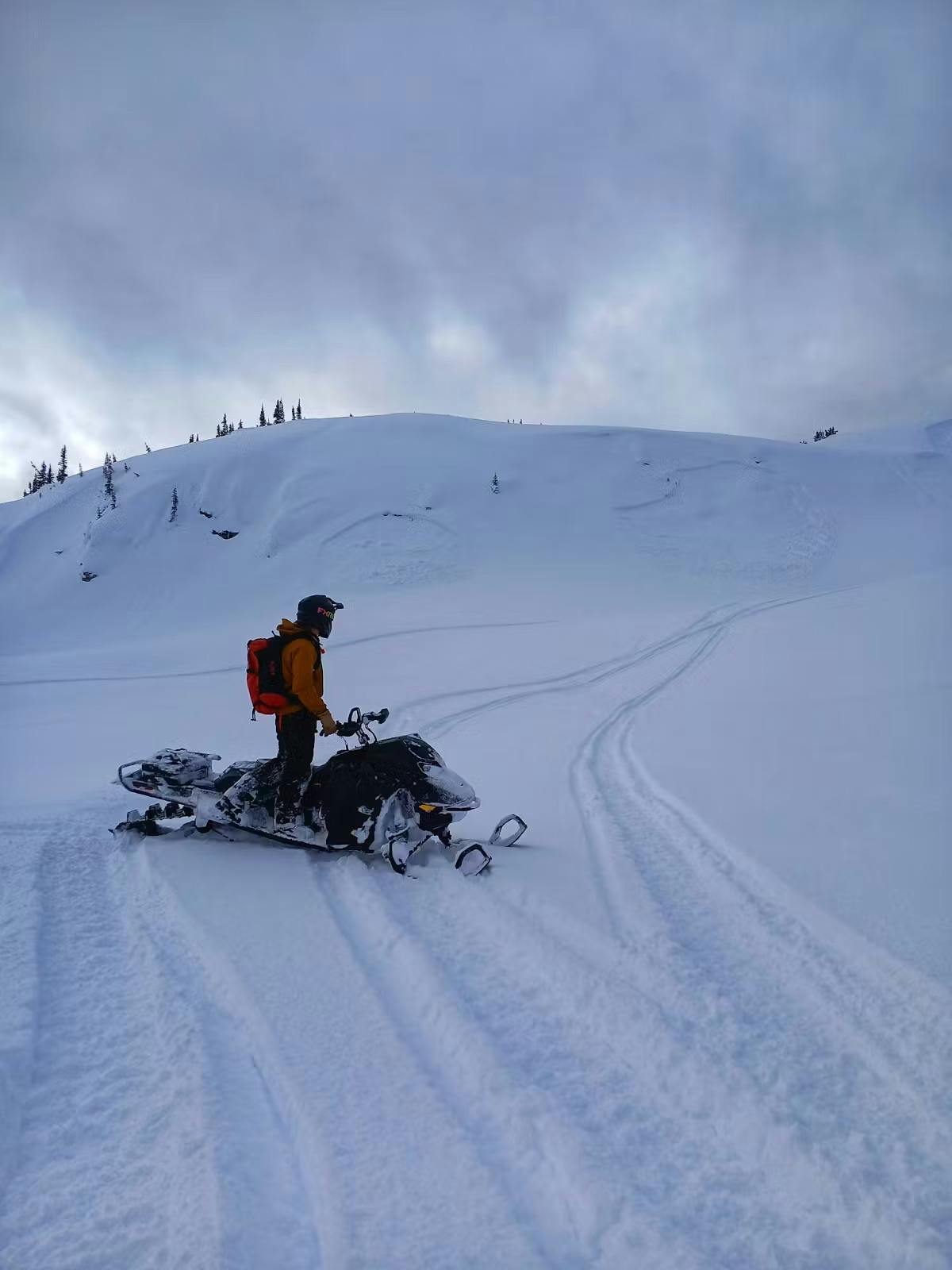 a person on a snowmobile looking at a small terrain feature that avalanched remotely