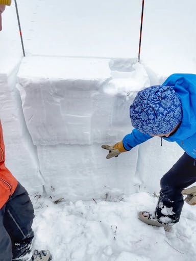 Snowpack test showing a failing layer mid-way down the block. A field tech points at it. 