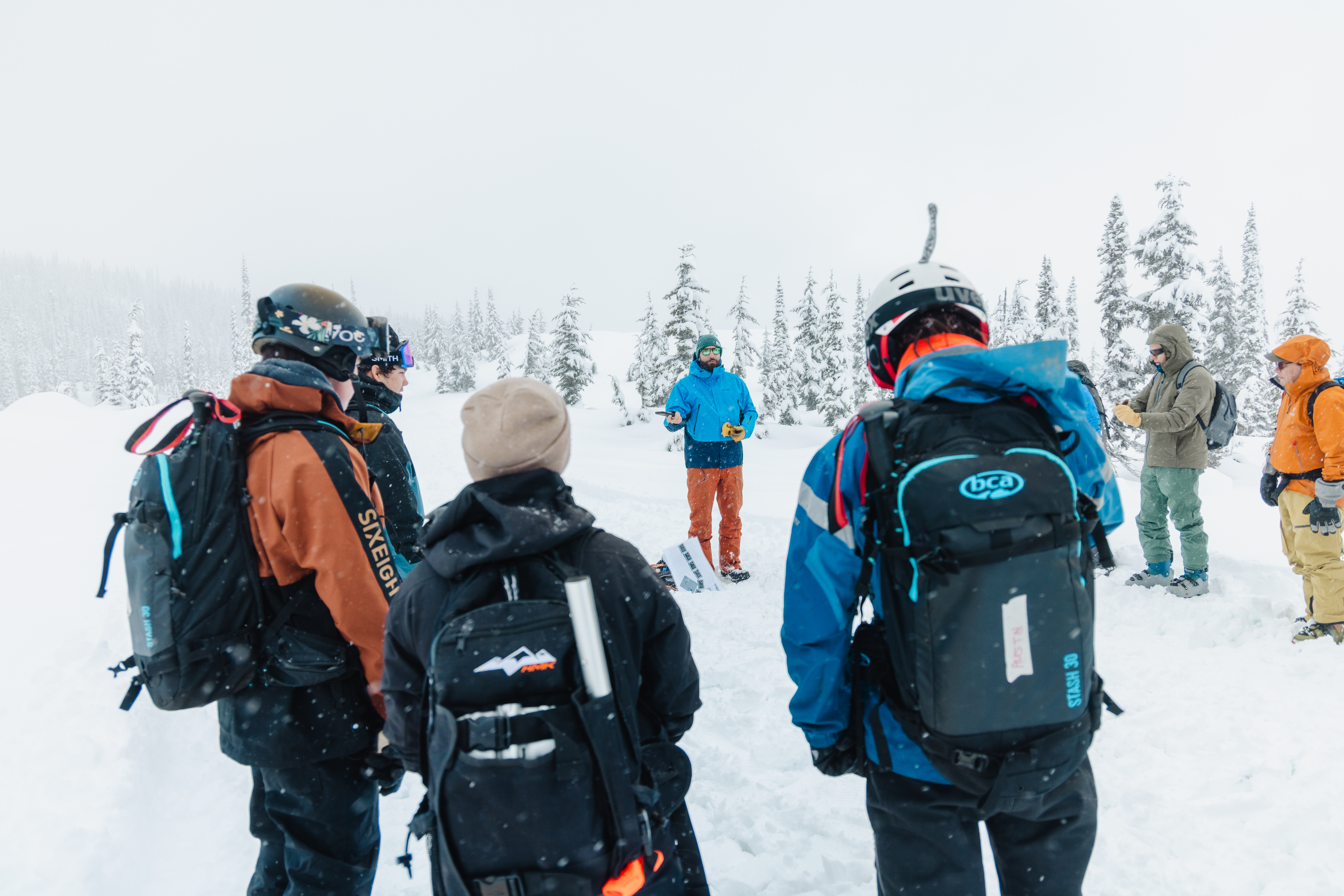 A group of people in outdoor wear standing in the snow listening to an instructor