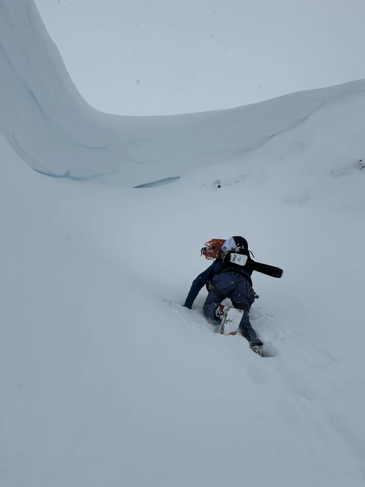 a skier bootpacking up a couloir with a looming cornice overhead