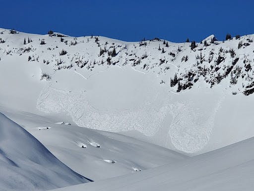 An avalanche on a sunny slope beneath a rocky outcrop