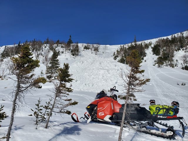 A snowmobile parked below an avalanche in Newfoundland.