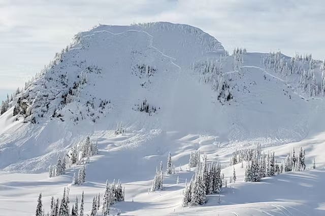 An alpine feature where sled tracks can be seen going up a steep slope. Above the tracks is a large avalanche crown.
