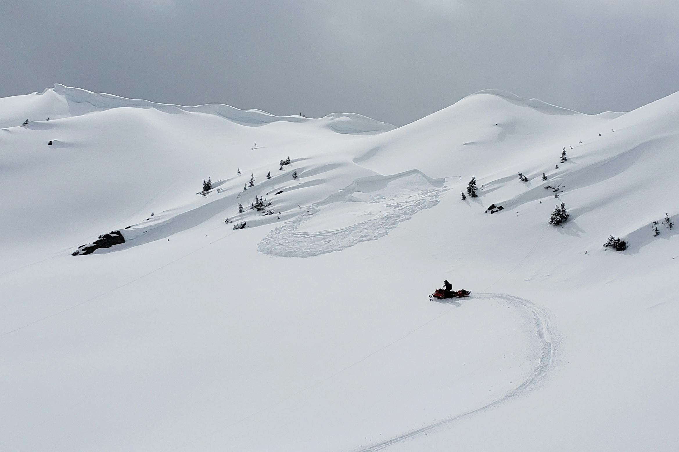A snowmobiler triggers an avalanche from a distance.