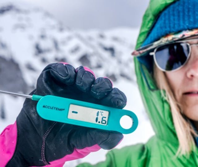 A field team member holds a thermometer showing 1.6 degrees on the screen.