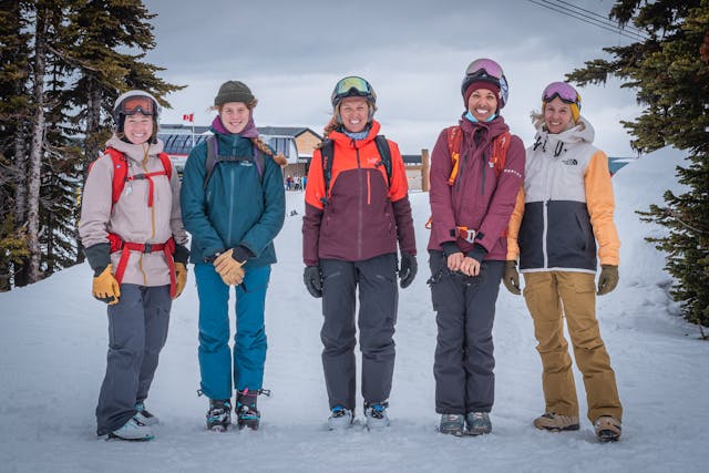 Five members of Mountain Mentors standing in front of a ski lift smiling at the camera. 