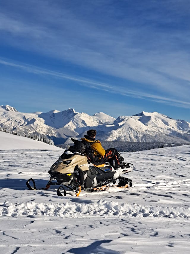 A member of an AvCan field team sits facing backwards on a stationary snowmobile, laying back against the seat and soaking up the sunshine.