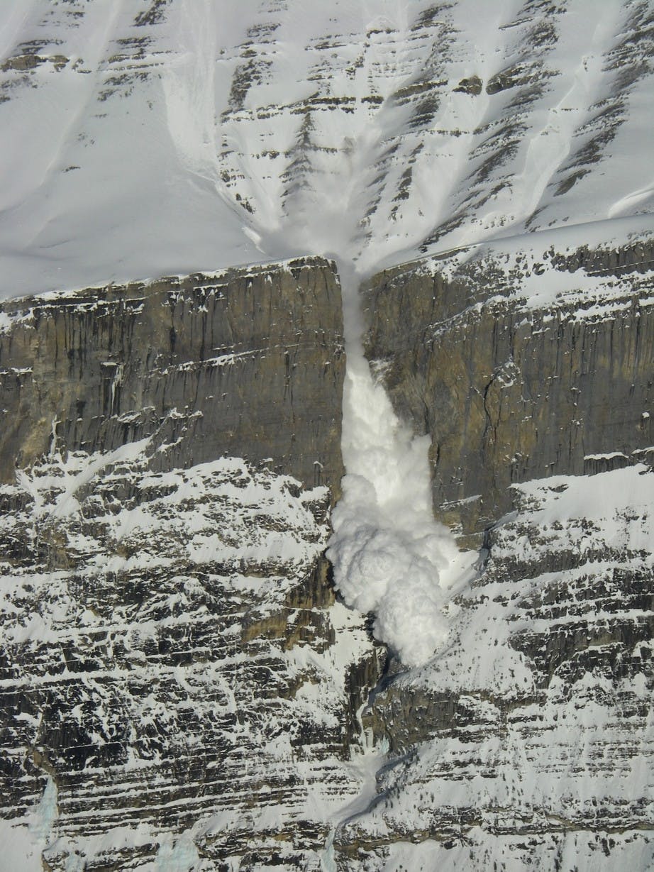 An avalanche flows over the waterfall, producing a large powder cloud that covers the whole climb.