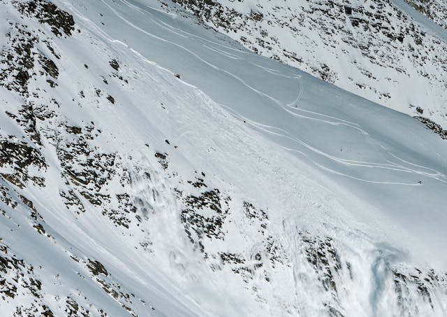 Image shows the aftermath of an avalanche running over some cliffs. There is a figure low on the right side of the image above said cliffs.