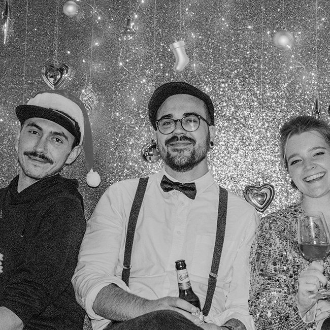 Drei Teammitglieder lächelnd vor der glitzernden Fotowand auf der Weihnachtsfeier