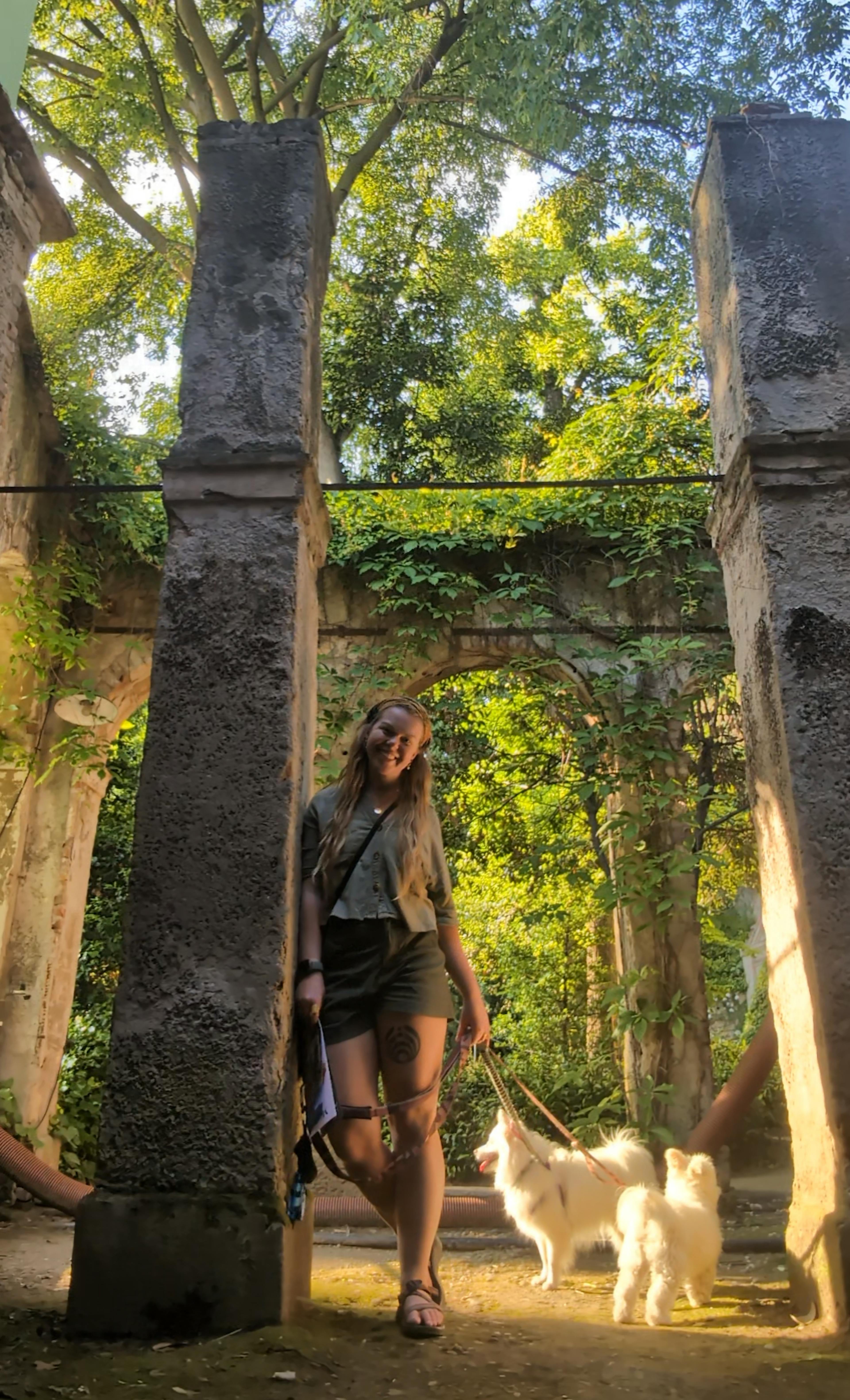 Ayse standing beside a stone column with her two pups