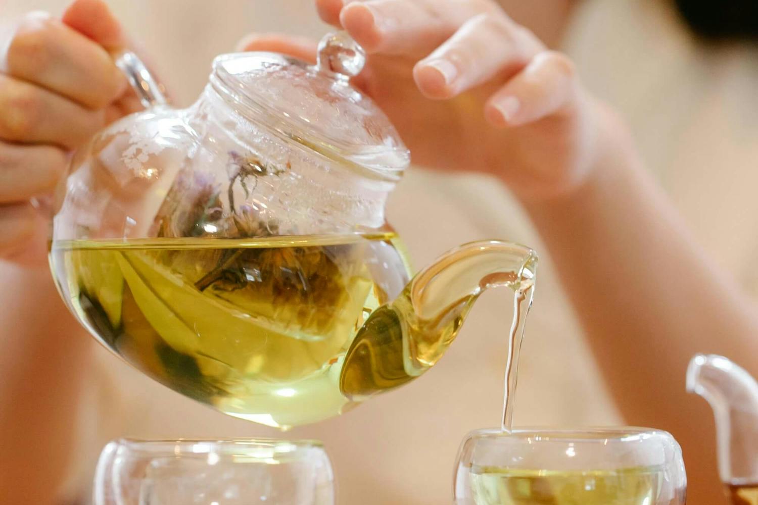 Frau schenkt Tee aus einer gläsernen Teekanne in Tassen ein Frau schenkt Tee aus einer gläsernen Teekanne in Tassen ein