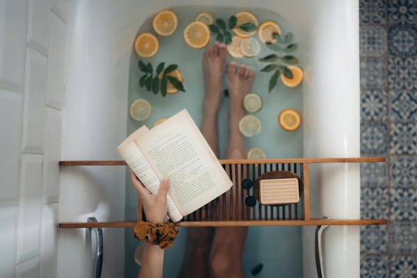 Frau sitzt mit Buch in Badewanne