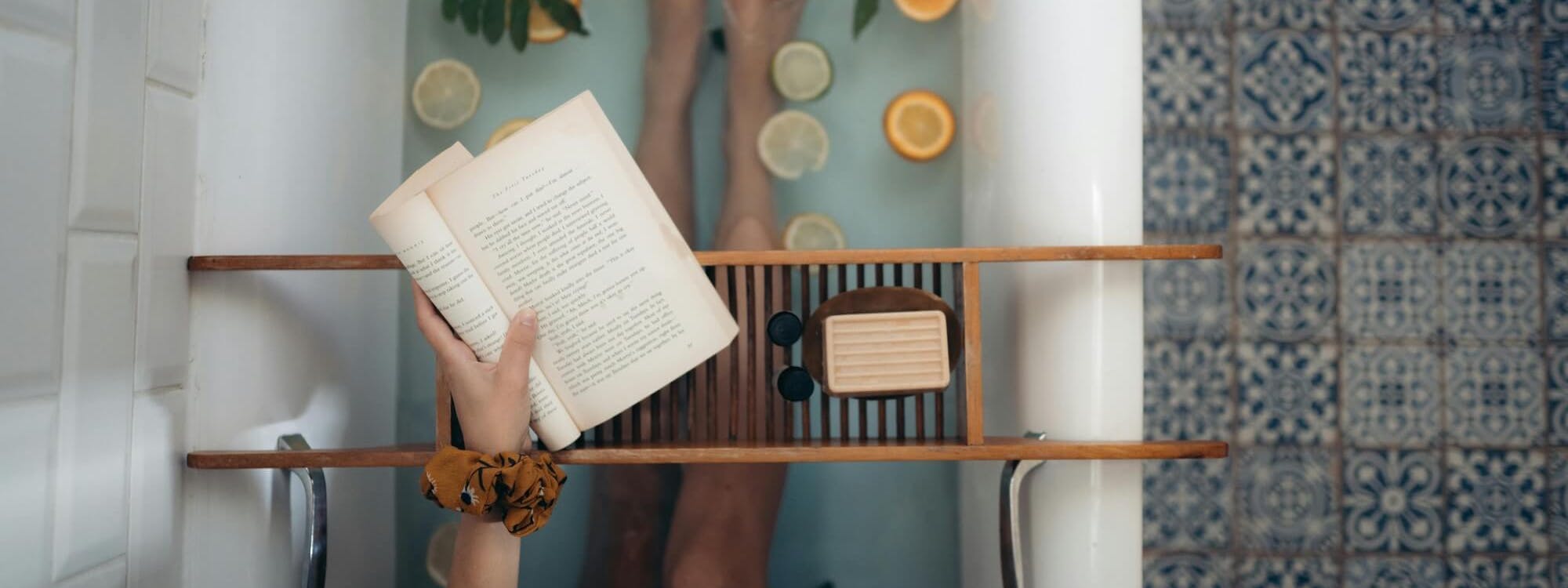 Frau sitzt mit Buch in Badewanne