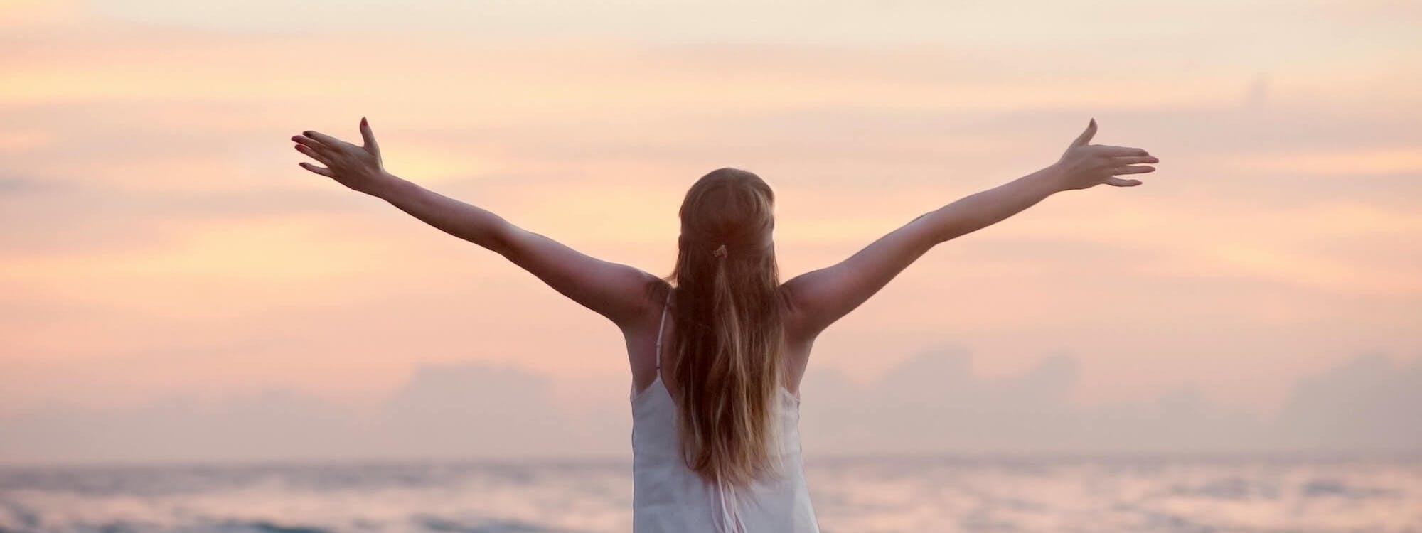 Frau steht mit offenen Armen vor dem Meer