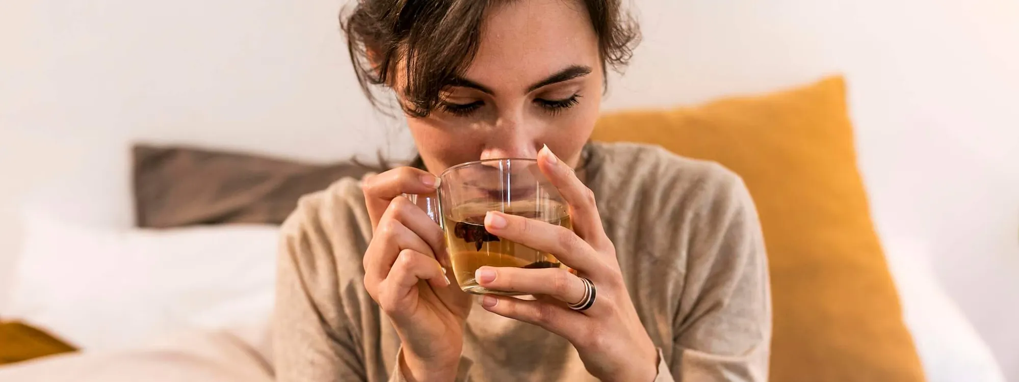 Frau sitzt auf ihrem Bett und trinkt Tee