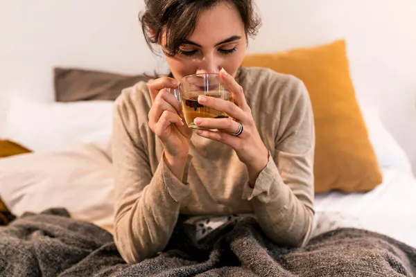 Frau sitzt auf ihrem Bett und trinkt Tee
