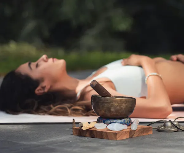 Frau liegt auf einer Yogamatte mit einer Klangschale vor sich