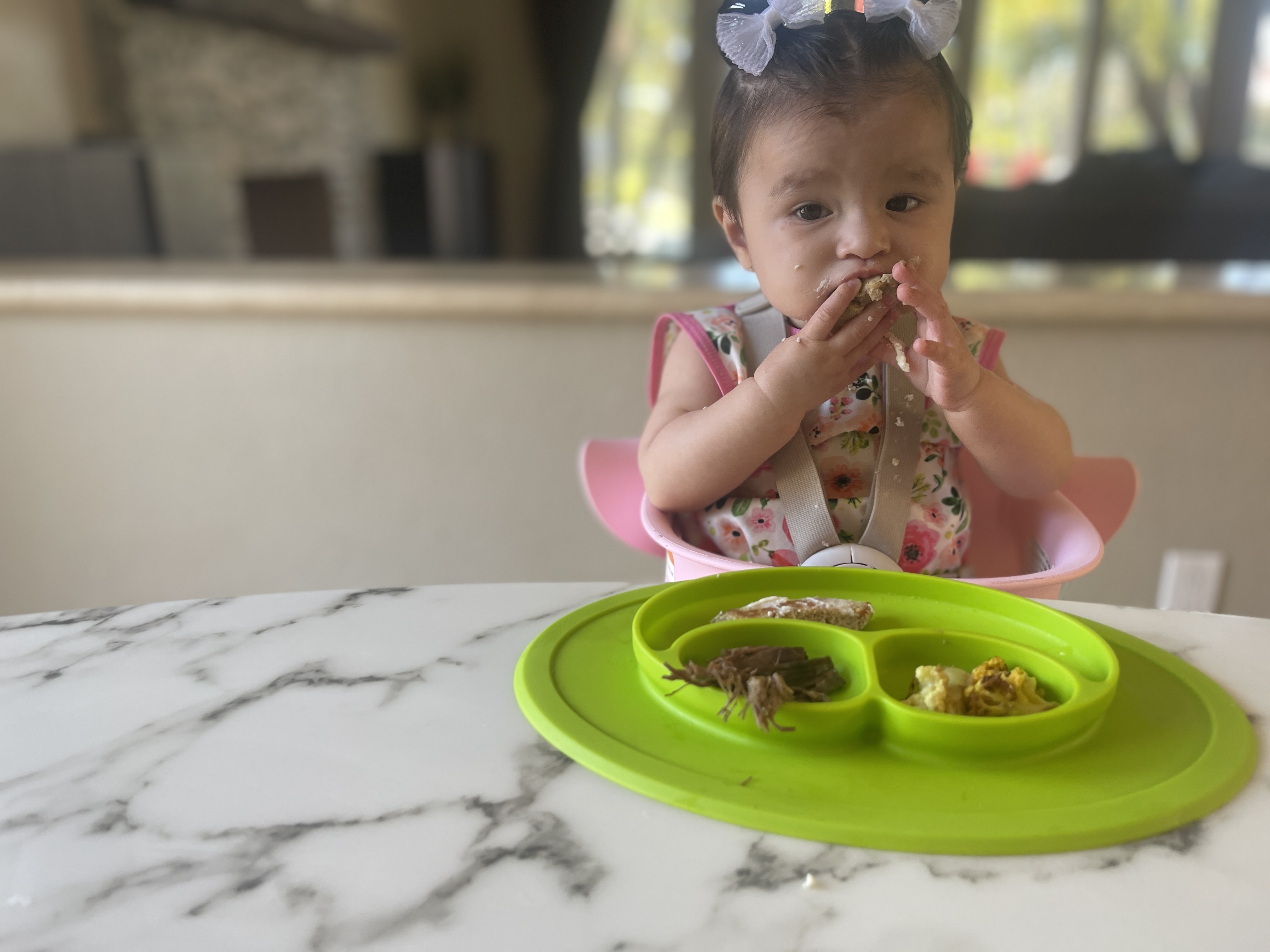 Photograph of baby seated in high chair with ezpz suction Mini Mat of food in front and she is brining food to her mouth