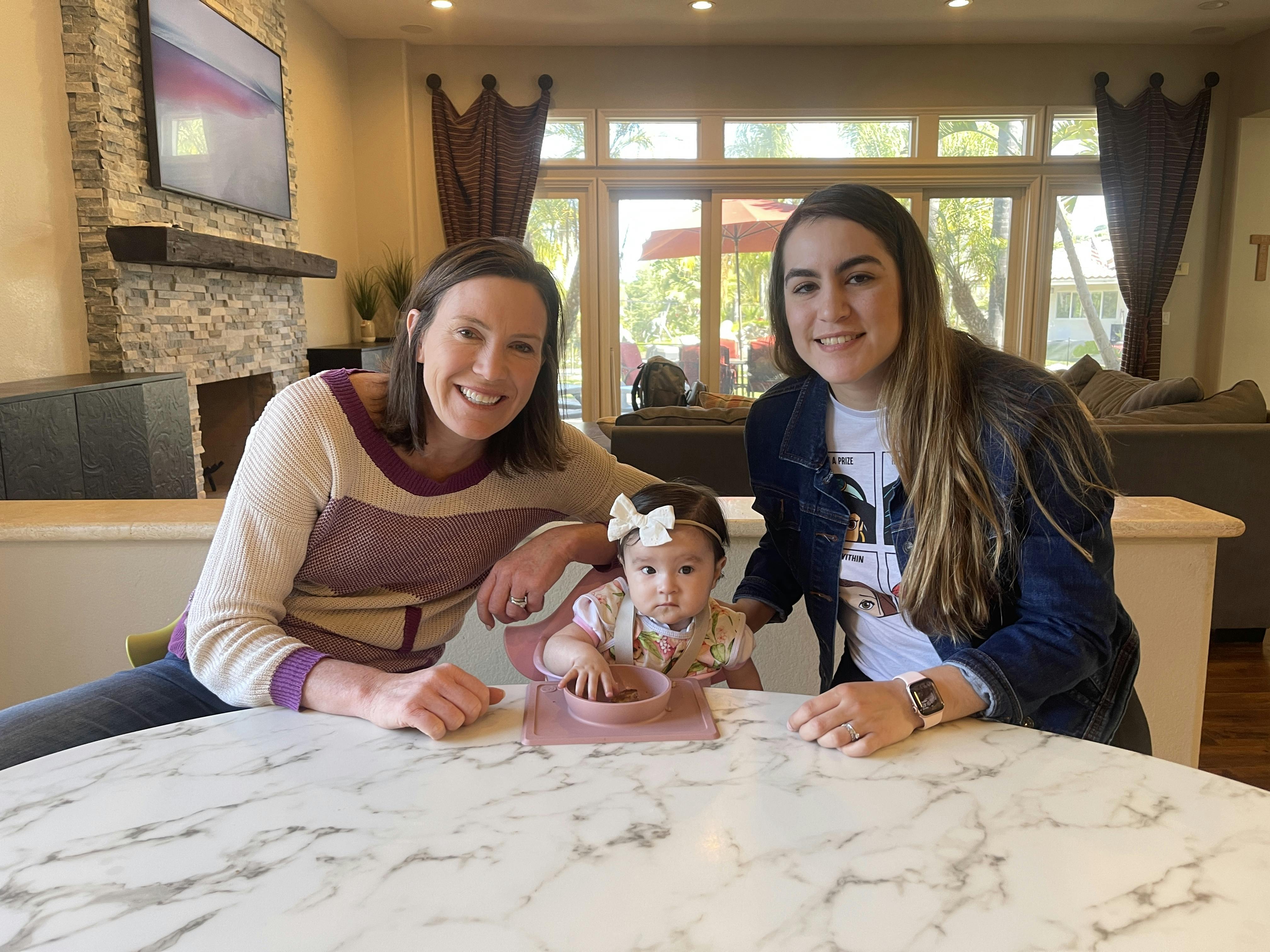 Dietitian Katie Ferraro, Alma and mom sitting at table with baby sitting in high chair and suction bowl of food in front of her