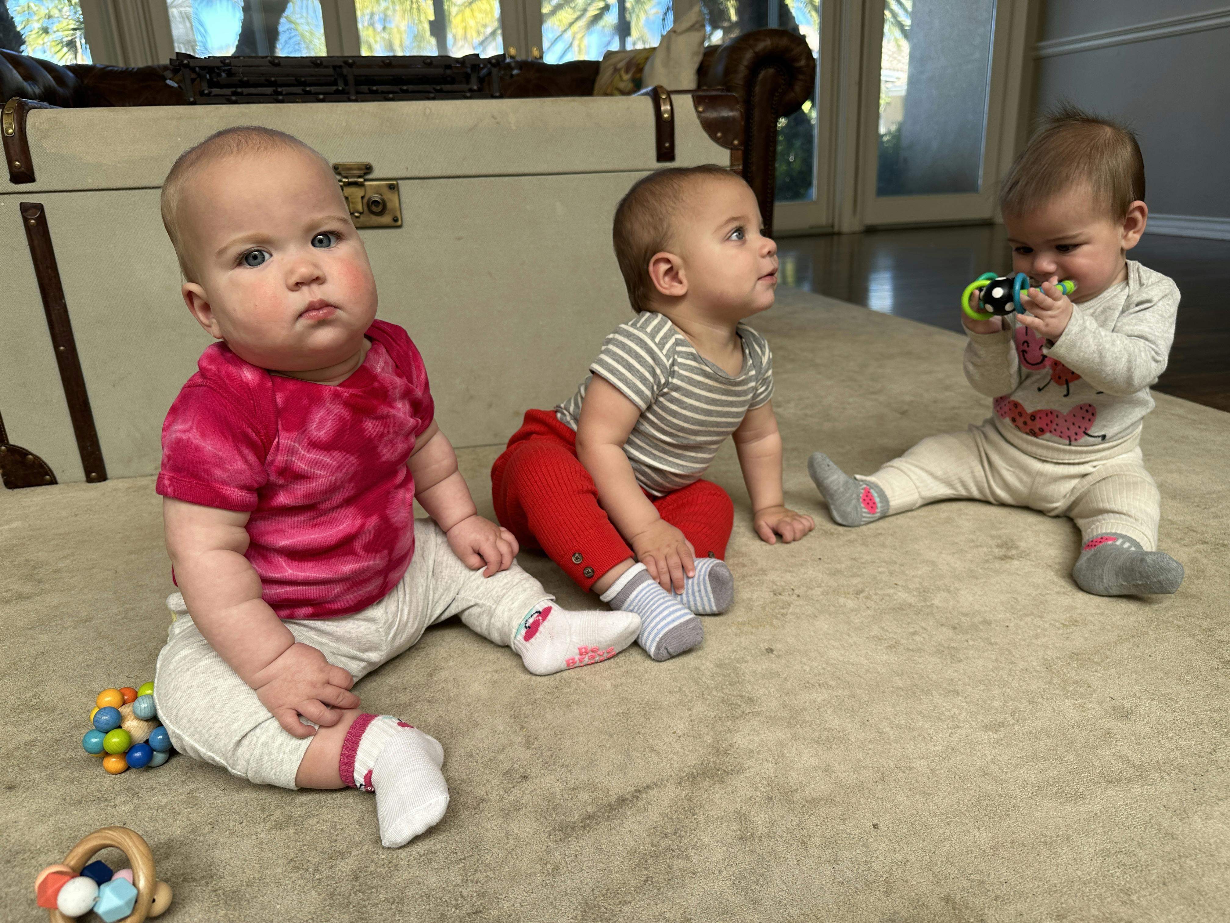 Triplet babies sitting by themsleves, unassisted on carpet