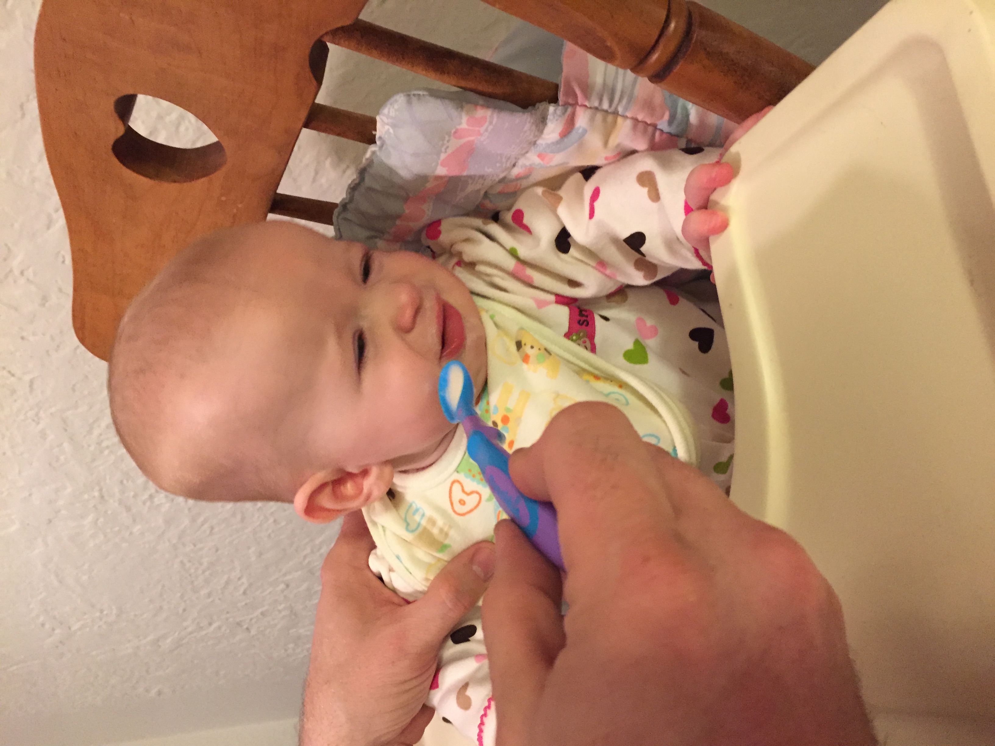 Baby in high chair turning her face away from a spoon of food being presented to her mouth by an adult hand