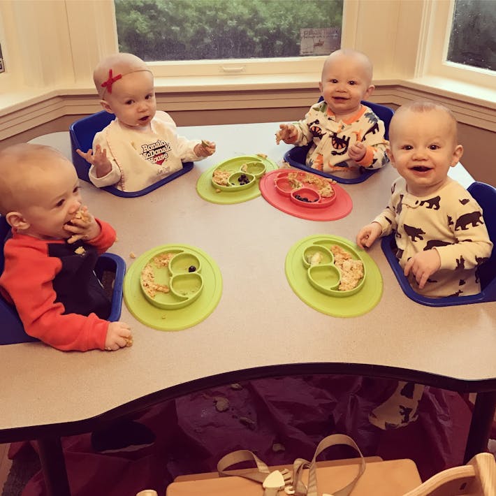 Photograph of quaduplet babies seated around a feeding table each with an ezpz suction Mini Mat with food in front of them.