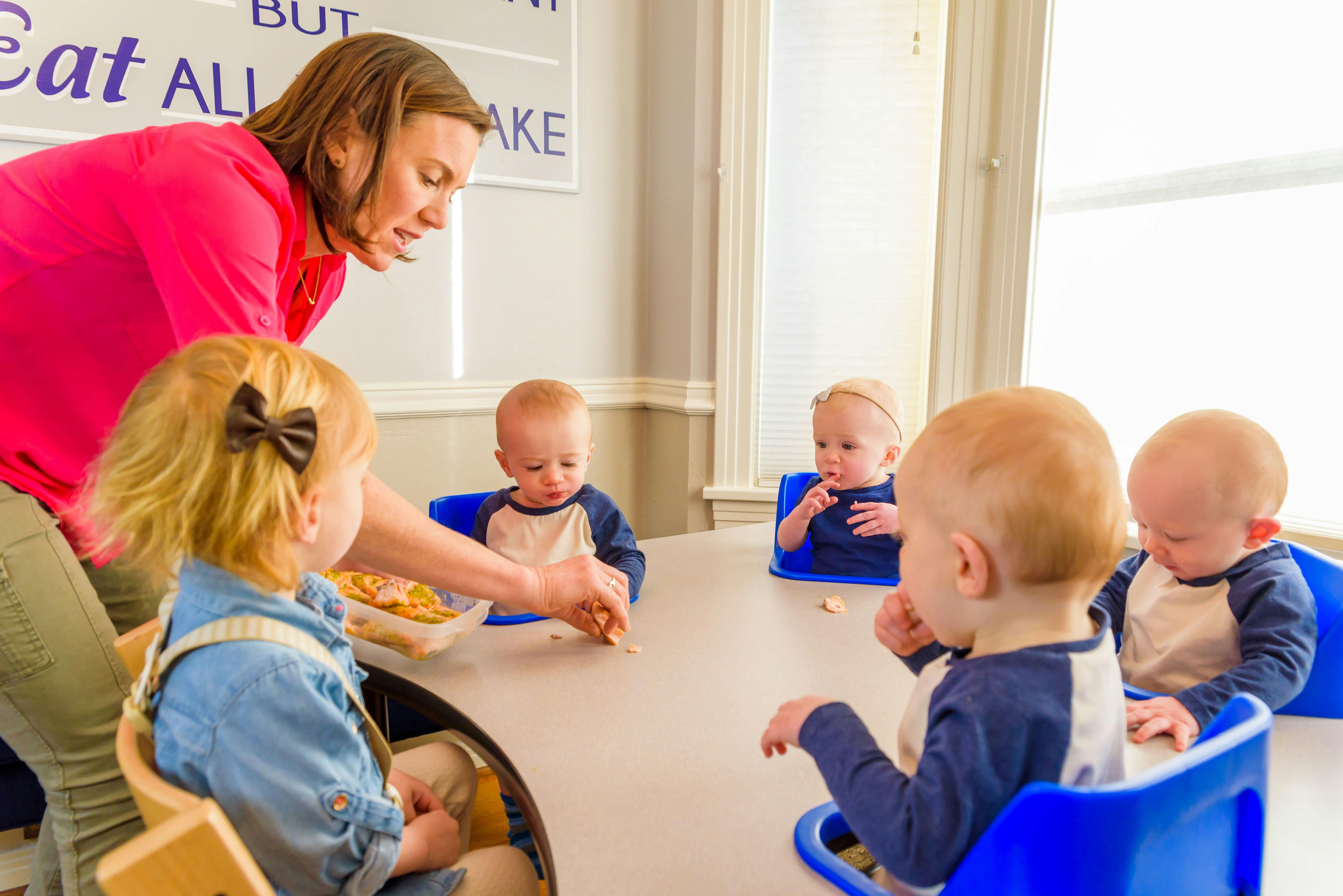 Katie Ferraro offering food to quadruplet babies in feeding table with toddler daughter in foreground