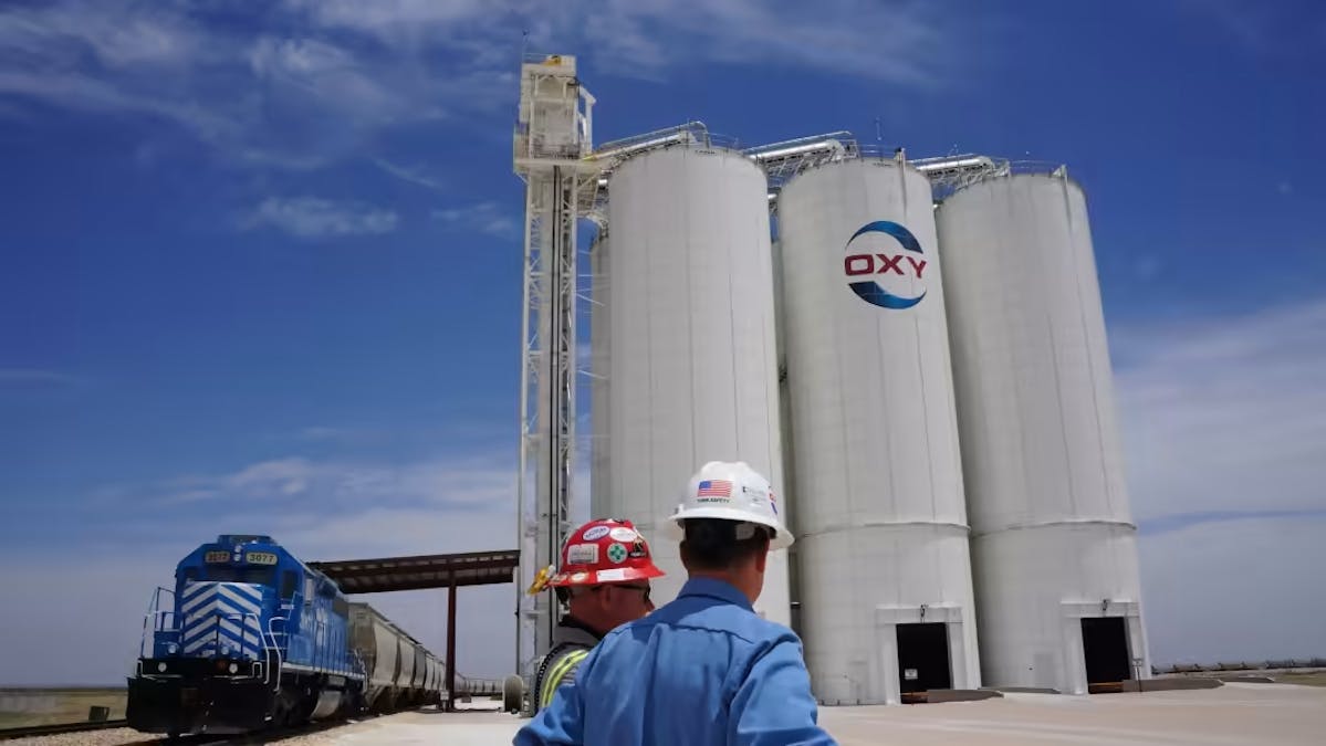 Oil workers look at oilfield equipment branded with Occidental Petroleum's "Oxy" logo