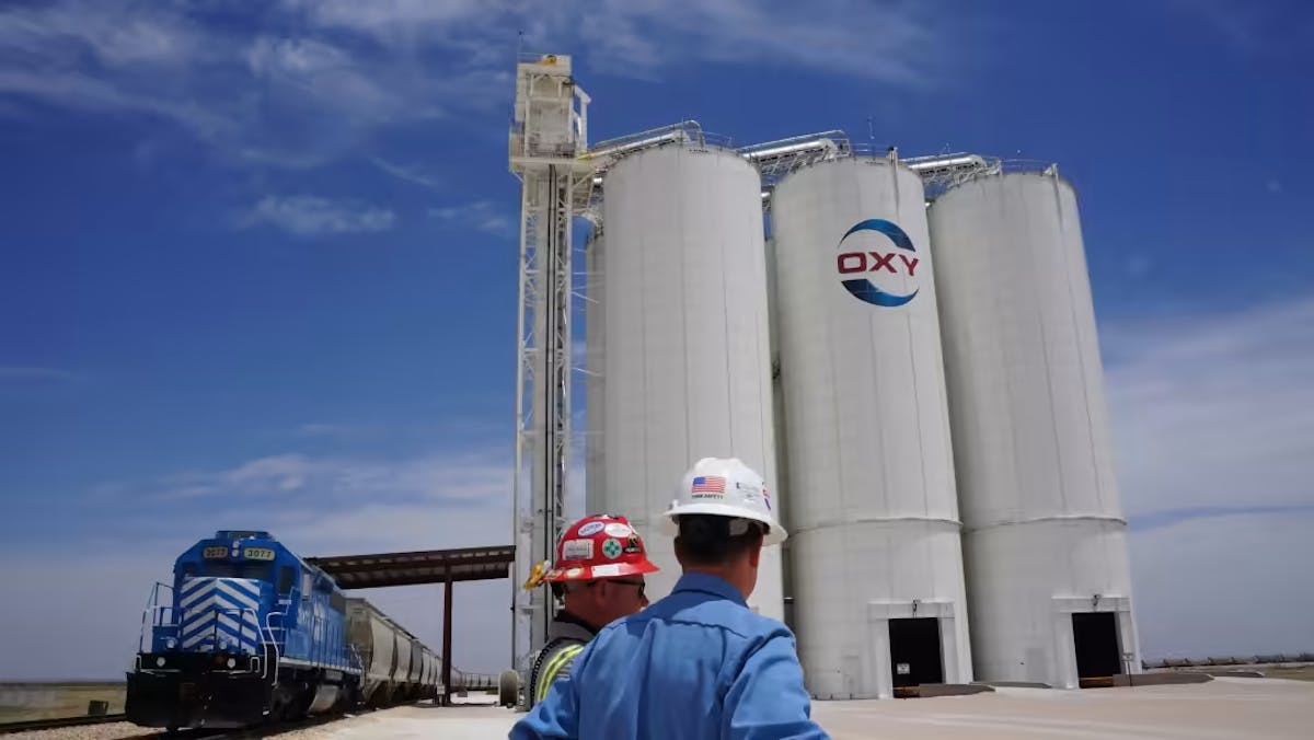 Oil workers looking at storage tanks emblazoned with the Occidental Petroleum logo