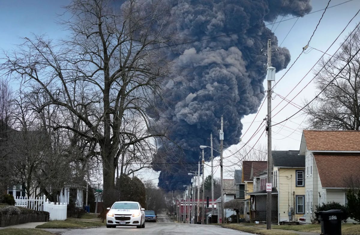 A suburban neighborhood with a big black cloud of smoke billowing in the distance
