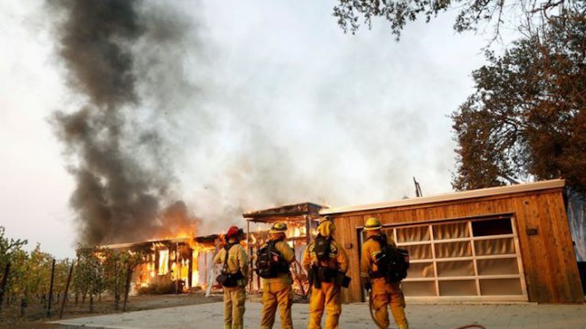 A group of firefighters look on as a house burns during the wind-driven Kincade Fire in Healdsburg, California