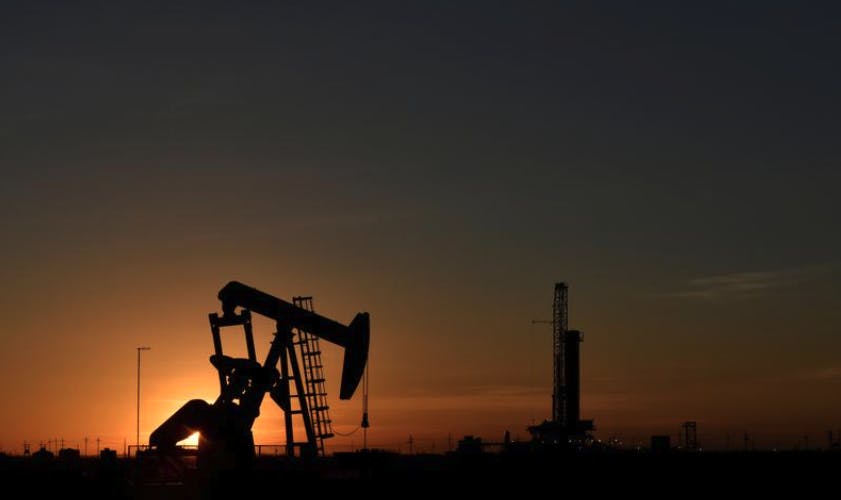 A pump jack operates in front of a drilling rig at sunset in an oil field in Midland, Texas U.S. August 22, 2018.  