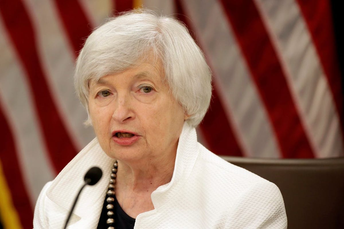 Treasury Secretary Janet Yellen talking into a microphone with flags behind her