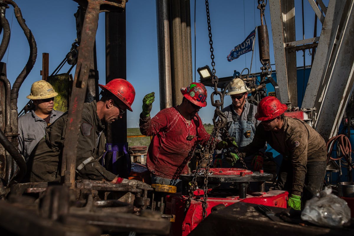 Five oil workers with safety hats on working on a rig