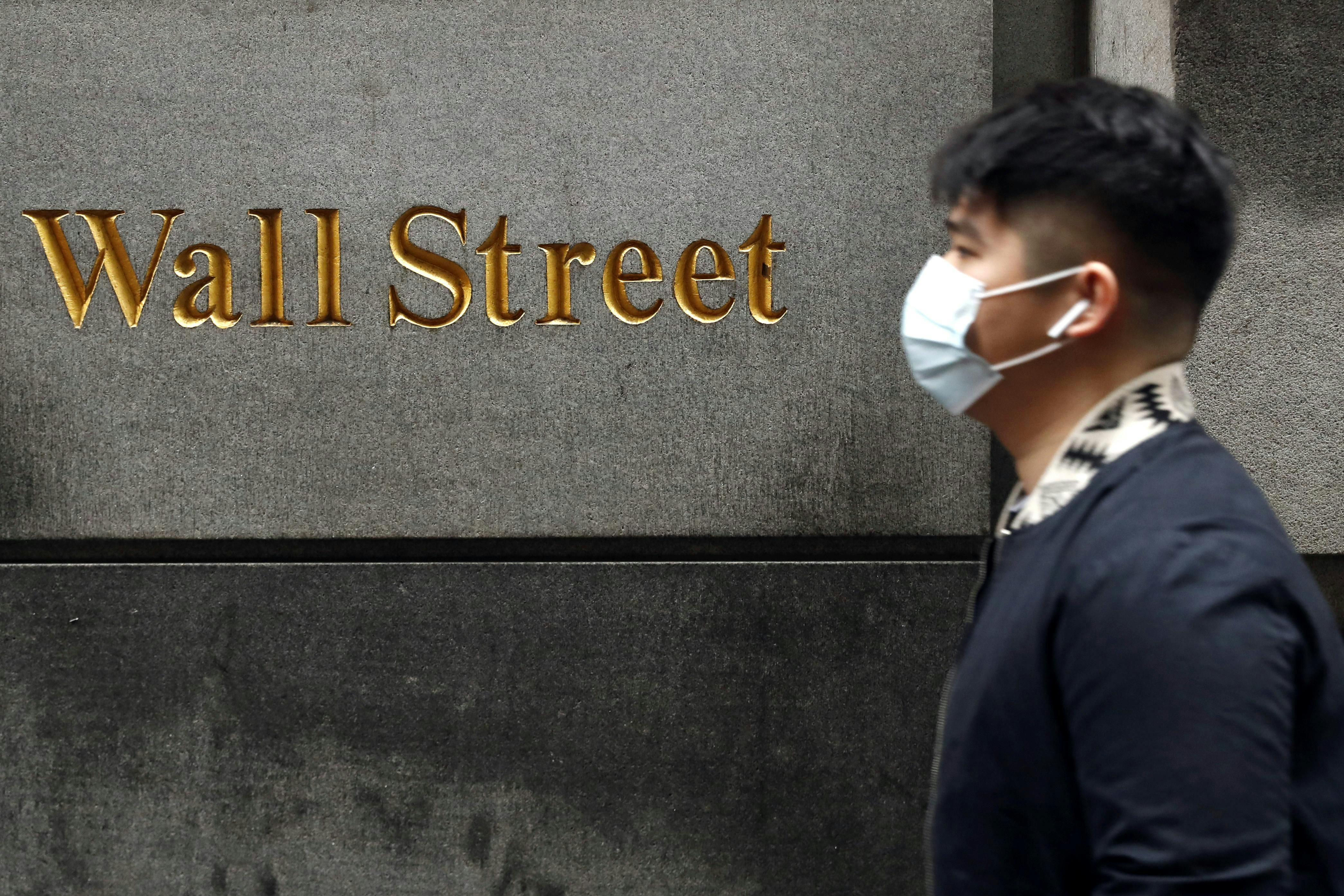 A man wearing a mask walks on Wall Street