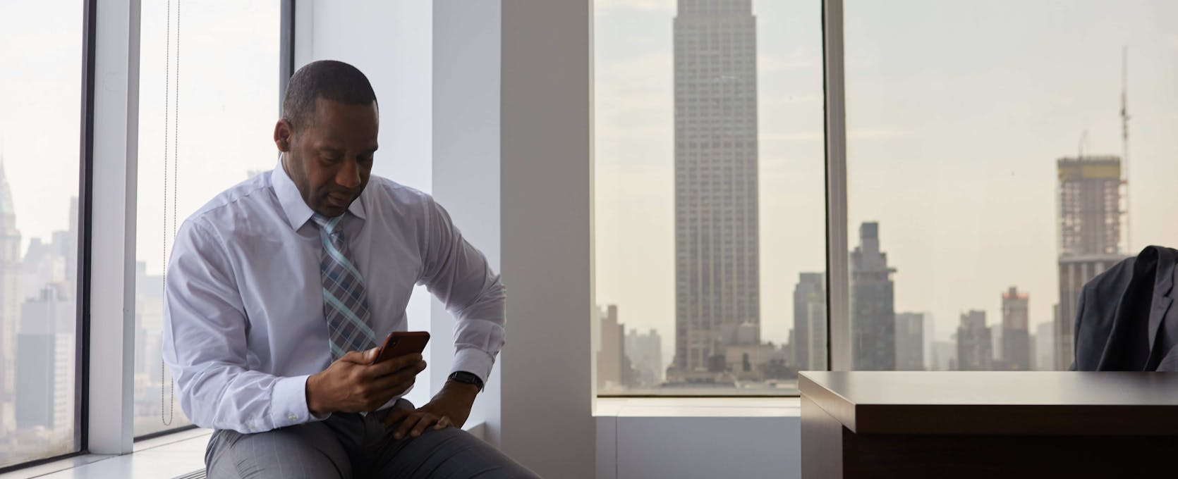 Man sitting at the window in his office while looking at his phone