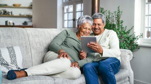 Mature couple sitting together on a couch looking at a tablet