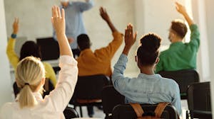 Students raising their hands in a university classroom