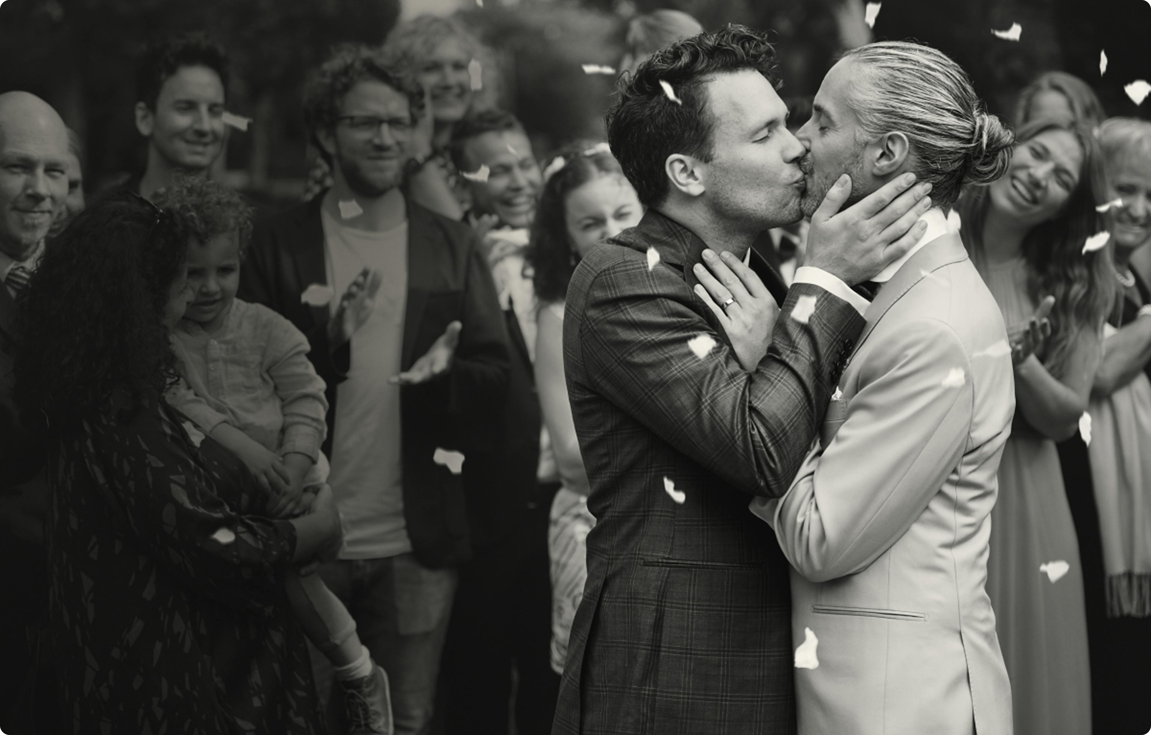 Schwarzweißbild von zwei Männern, die sich auf ihrer Hochzeit küssen.
