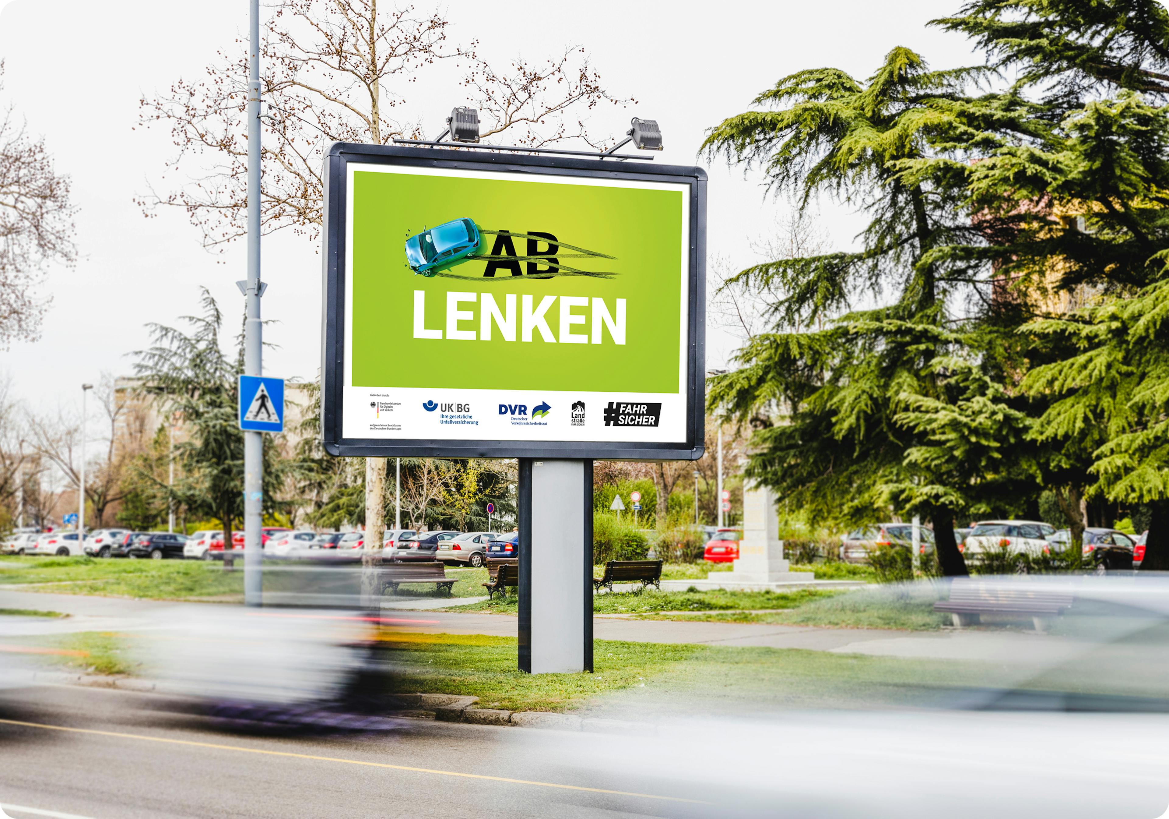 Ein Plakat mit der Aufschrift "Ablenken". Auf dem "Ab" sind Bremsspuren, darüber ein driftendes Auto.
