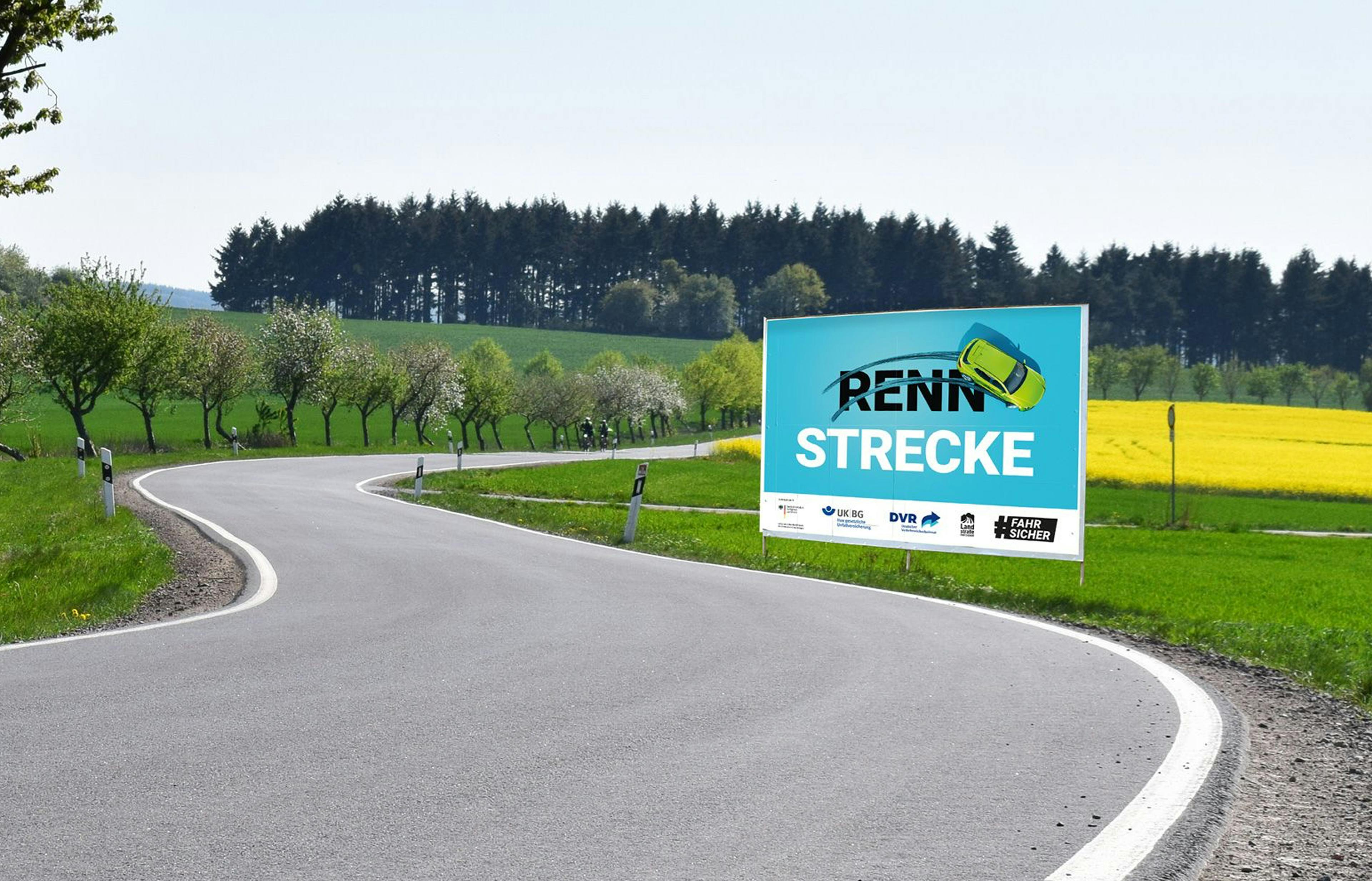 Ein Plakat mit dem Schriftzug "Rennstrecke" steht an einer Straße. Über dem "Renn" sind Bremsspuren, darüber driftet ein Auto.
