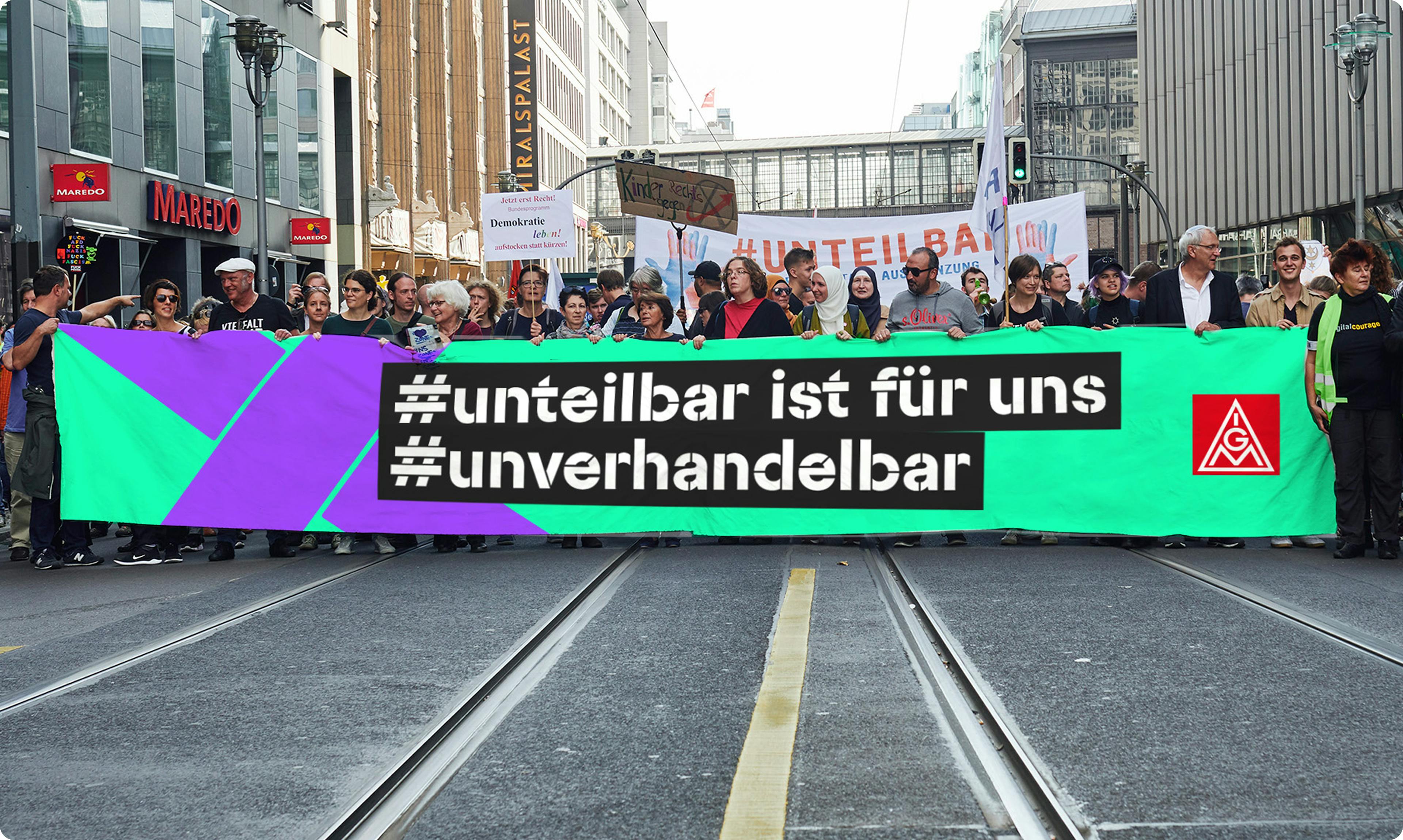 Frontales Bild eines Demonstrationszuges, im Vordergrund großes Banner mit der Aufschrift "#unteilbar ist für uns #unverhandelbar".