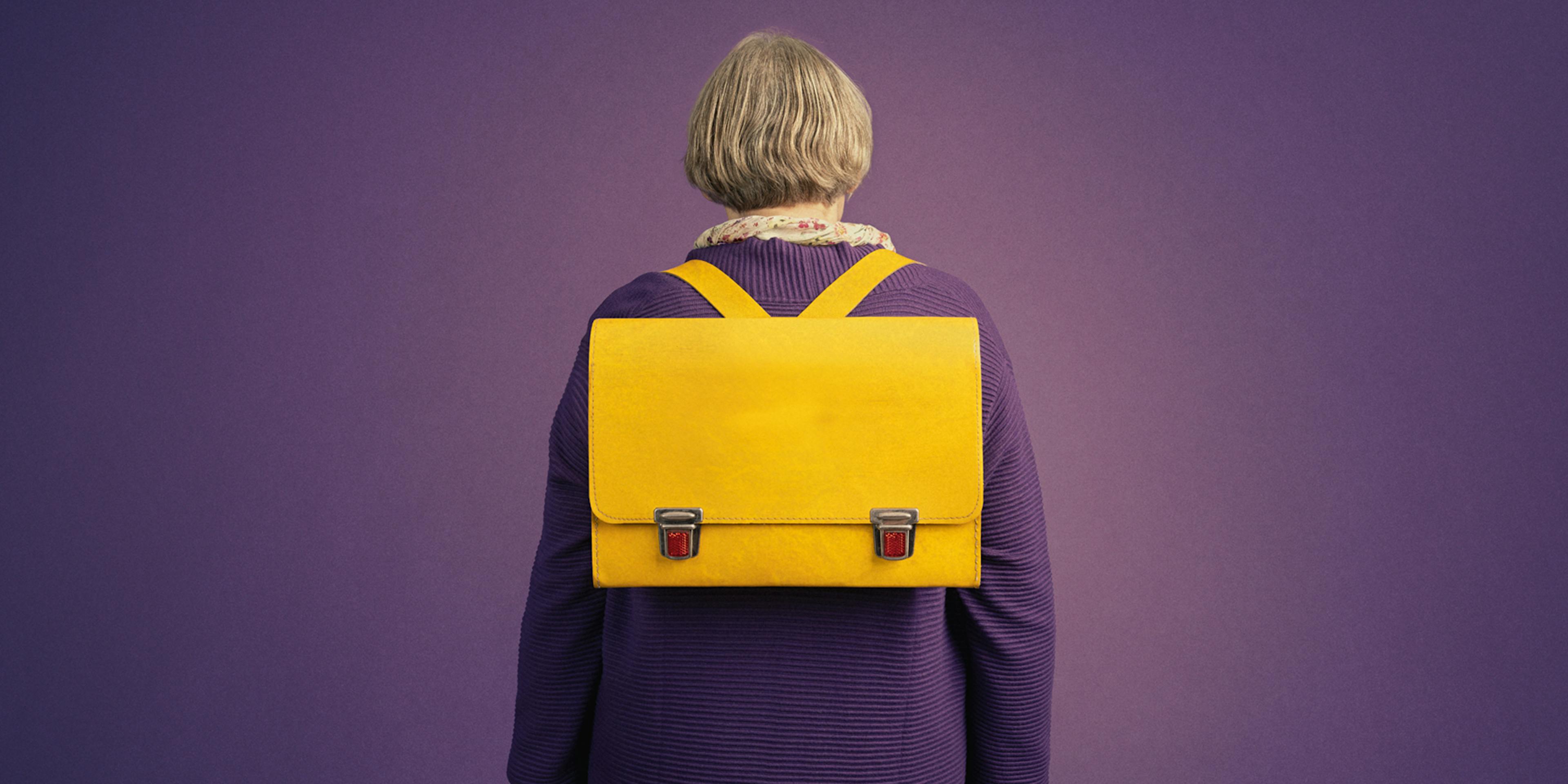 Eine ältere Frau mit Schulrucksack von hinten fotografiert.